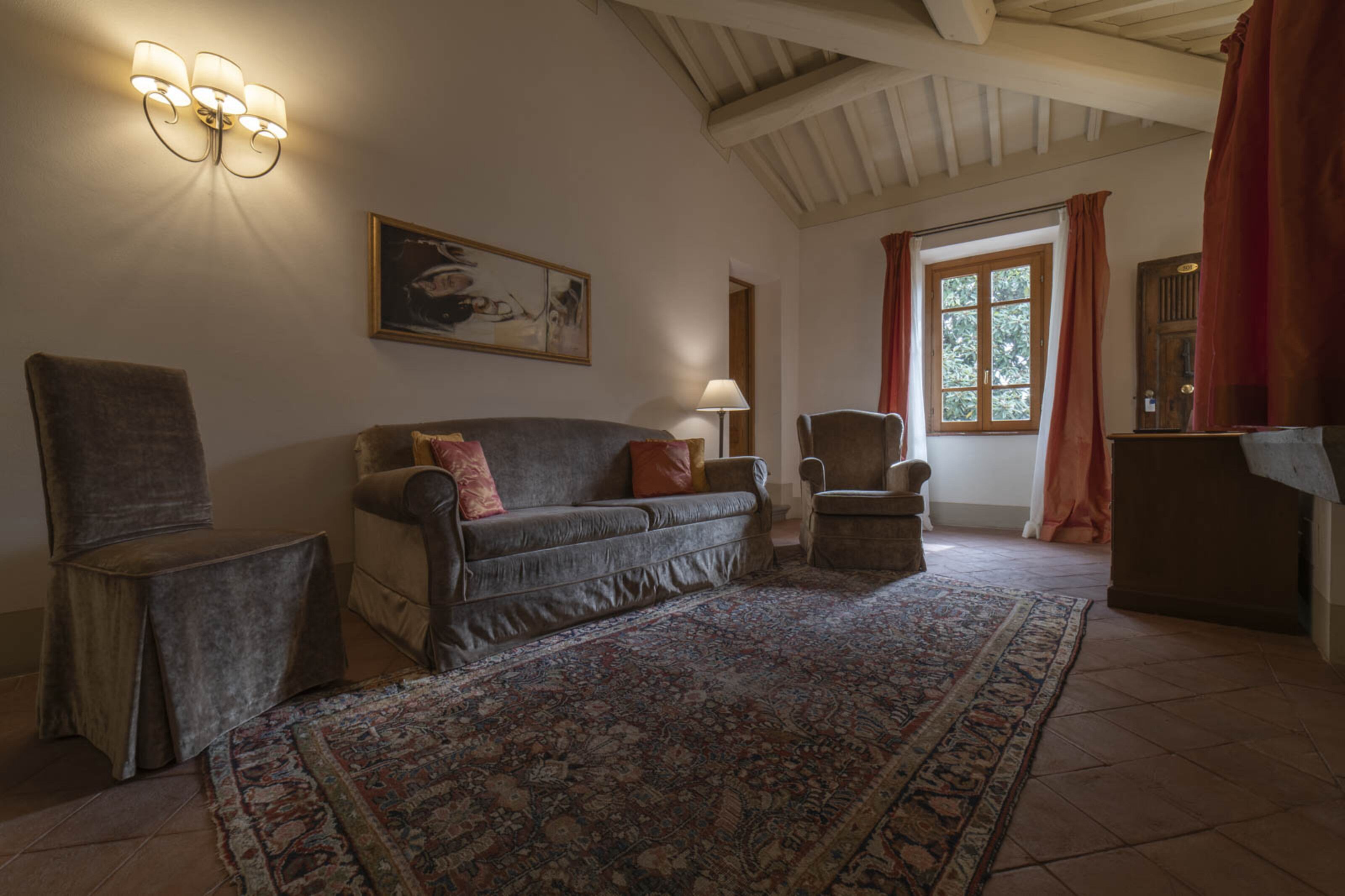 Een gezellige woonkamer met een bank, fauteuils, een vloerkleed en een schilderij aan de muur.