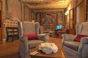 Una habitación con dos sillones, una mesa de centro con un ramillete de flores blancas, un televisor y una estantería.