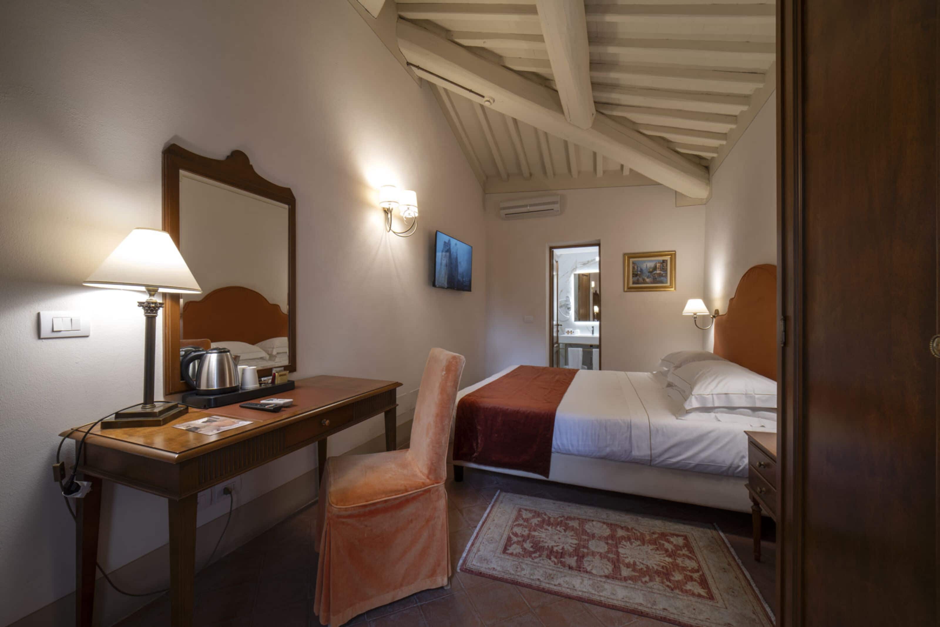 Een hotelkamer met een bed, een bureau, een stoel, een lamp, een schilderij en een deur.