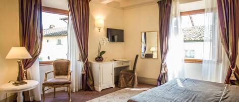 A hotel room with a bed, desk, chair, and a small table with a lamp.