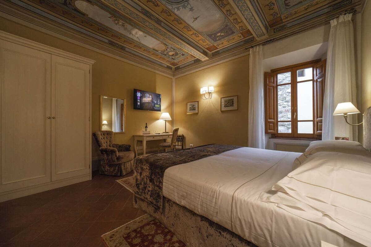 A bedroom with a large bed, a desk with a chair, a television, and a ceiling with intricate designs.