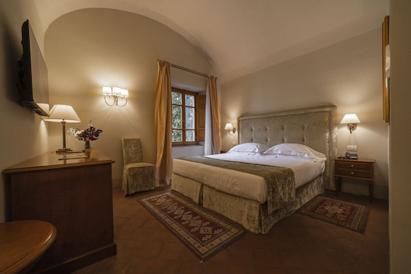 A bedroom with a large bed, a desk, a chair, and a TV.
