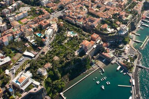 Vista aérea de uma cidade costeira com edifícios históricos, um porto de iates e uma estrutura fortificada.