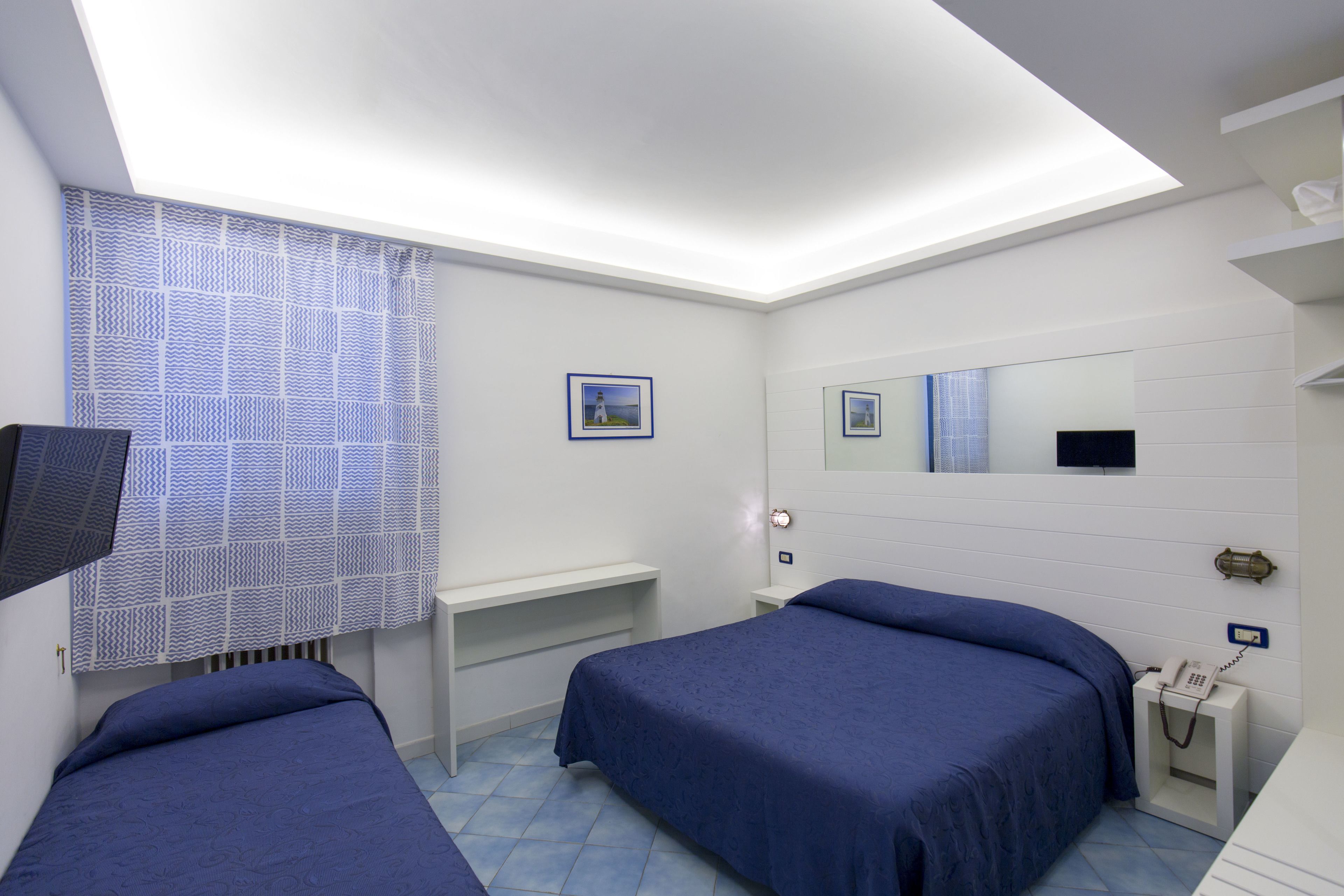 A bedroom with two beds, a desk, a mirror, and a telephone.