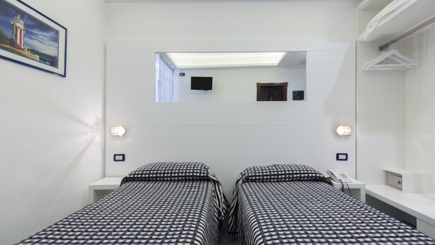 A hotel room with two beds, a skylight, a television, and a mirror.