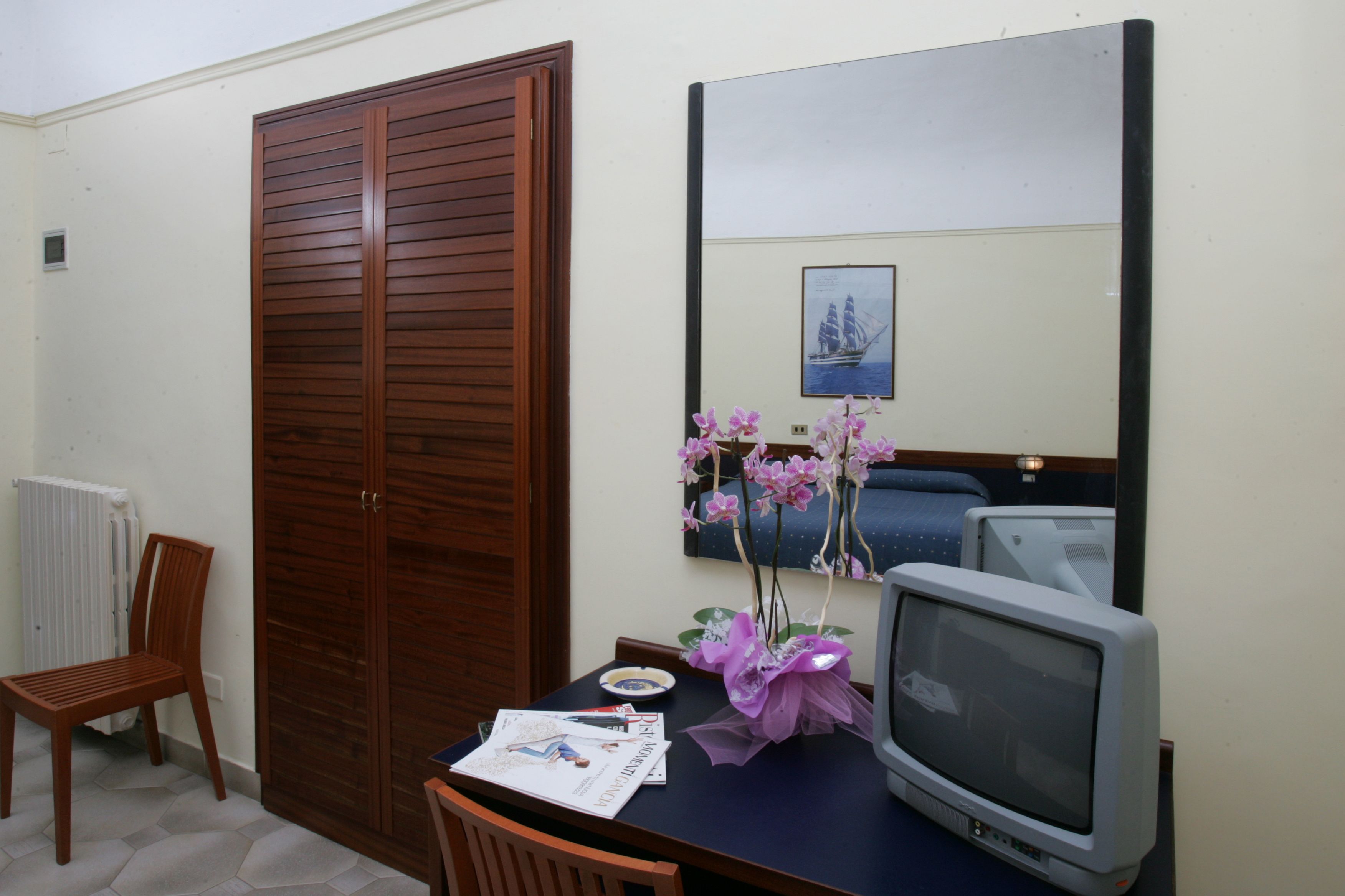 Una habitación con un armario de madera, televisor, una mesa con un florero y un cuadro en la pared.