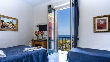 Una habitación con dos camas, un escritorio con una silla, un televisor y un balcón con vista al mar.