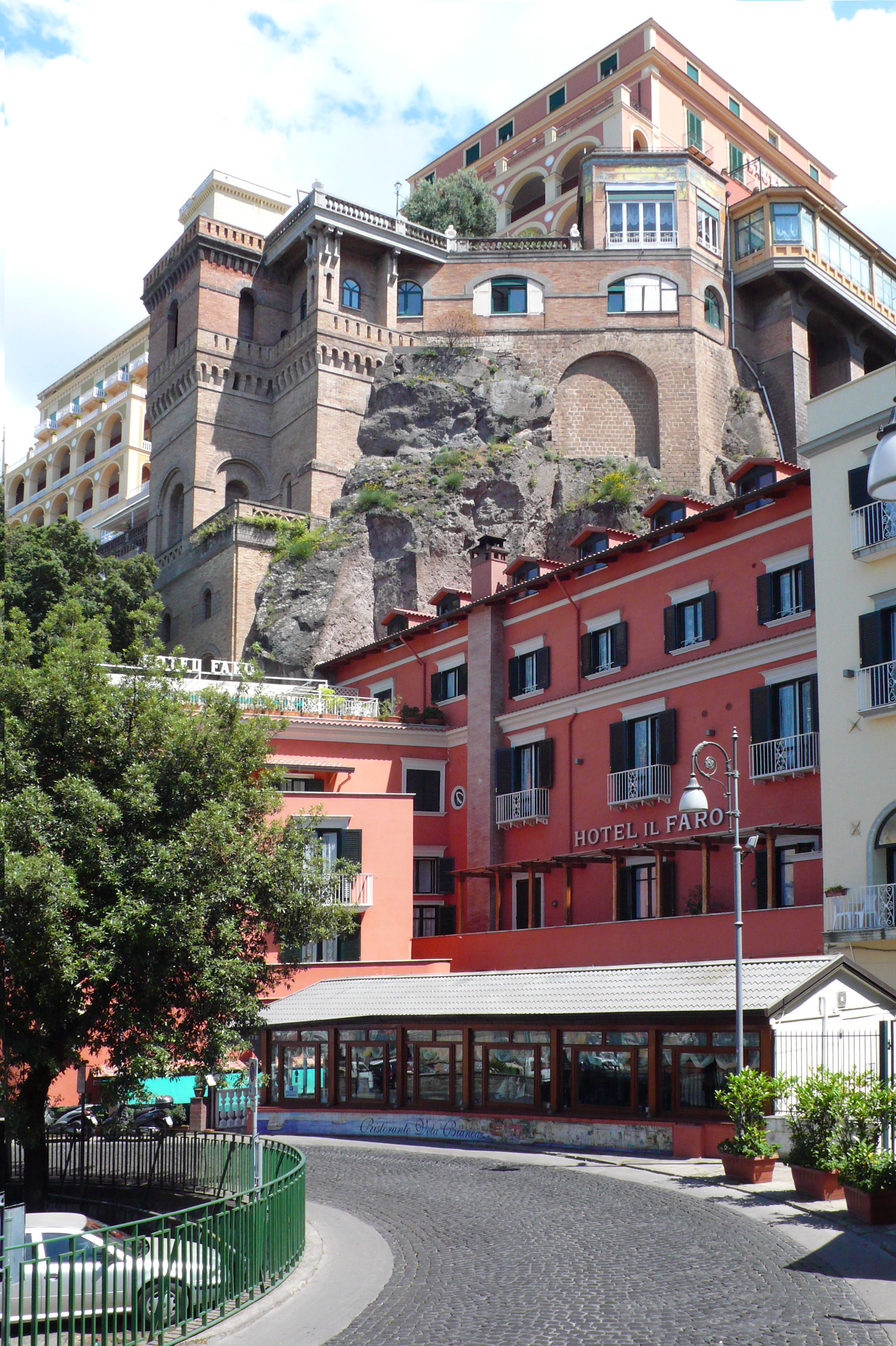 A hotel with a red facade, a balcony, and a view of a rocky cliff.
