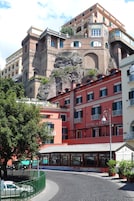 Un hotel con fachada roja, un balcón y vistas a un acantilado rocoso.