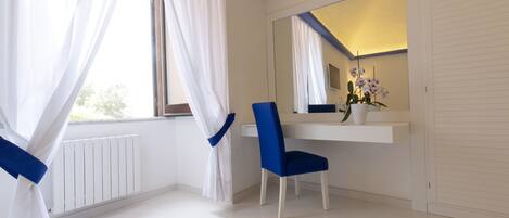 A modern bathroom with a white vanity, a blue chair, a large mirror, and a potted orchid.