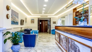 A hotel lobby with a reception desk, blue seating area, and a potted plant.