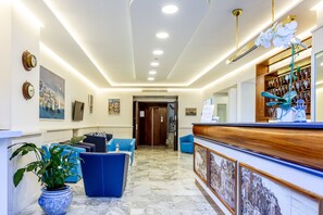 A hotel lobby with a reception desk, blue seating area, and a potted plant.