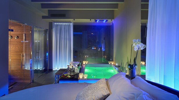 Une chambre d’hôtel moderne dotée d’un grand lit, d’un jacuzzi entouré de parois de verre et offrant une vue sur le ciel nocturne.