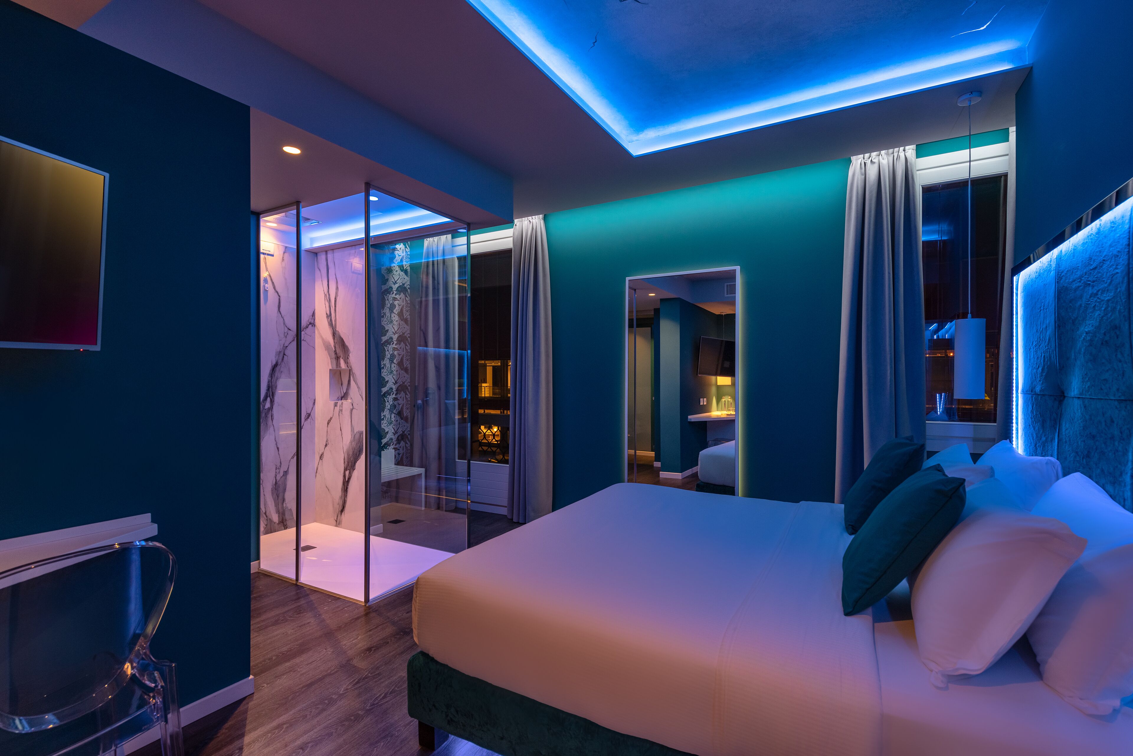 A modern hotel room with a large bed, a glass shower enclosure, and a view of the city.