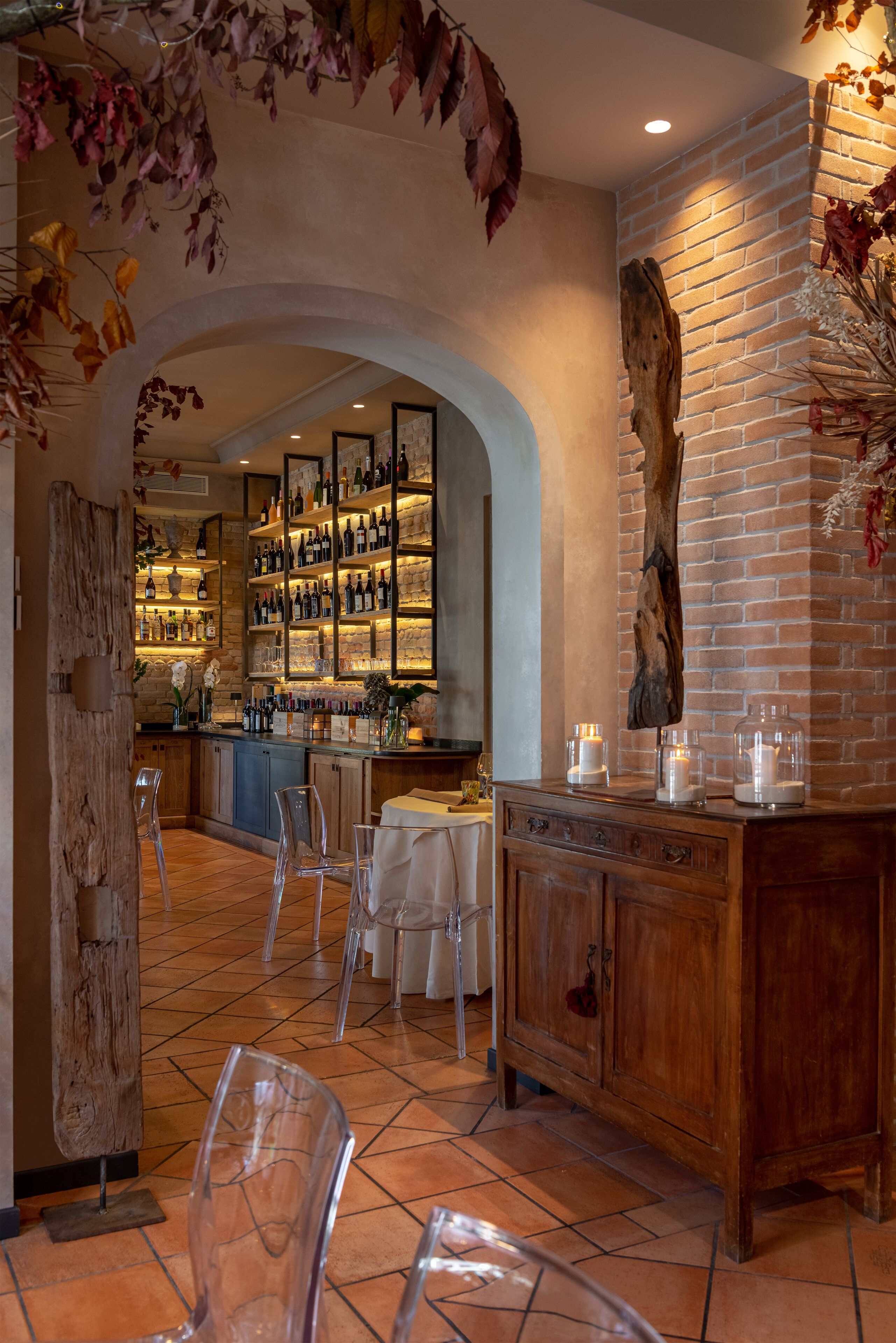 Zona de bar con pared de ladrillo, estanterías de madera con botellas y decoración rústica.