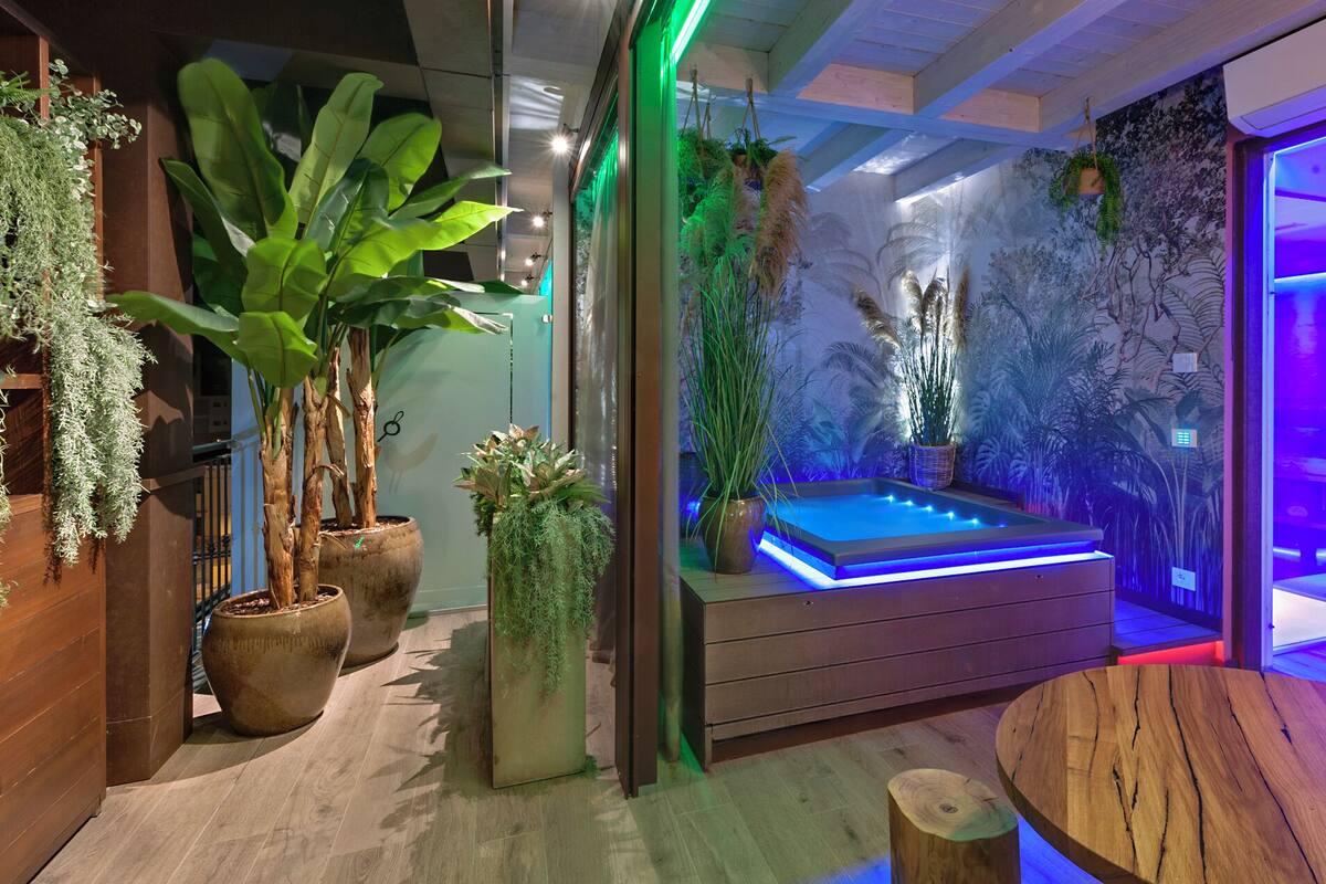A spa area with a hot tub, surrounded by large potted plants and a mural of tropical foliage.