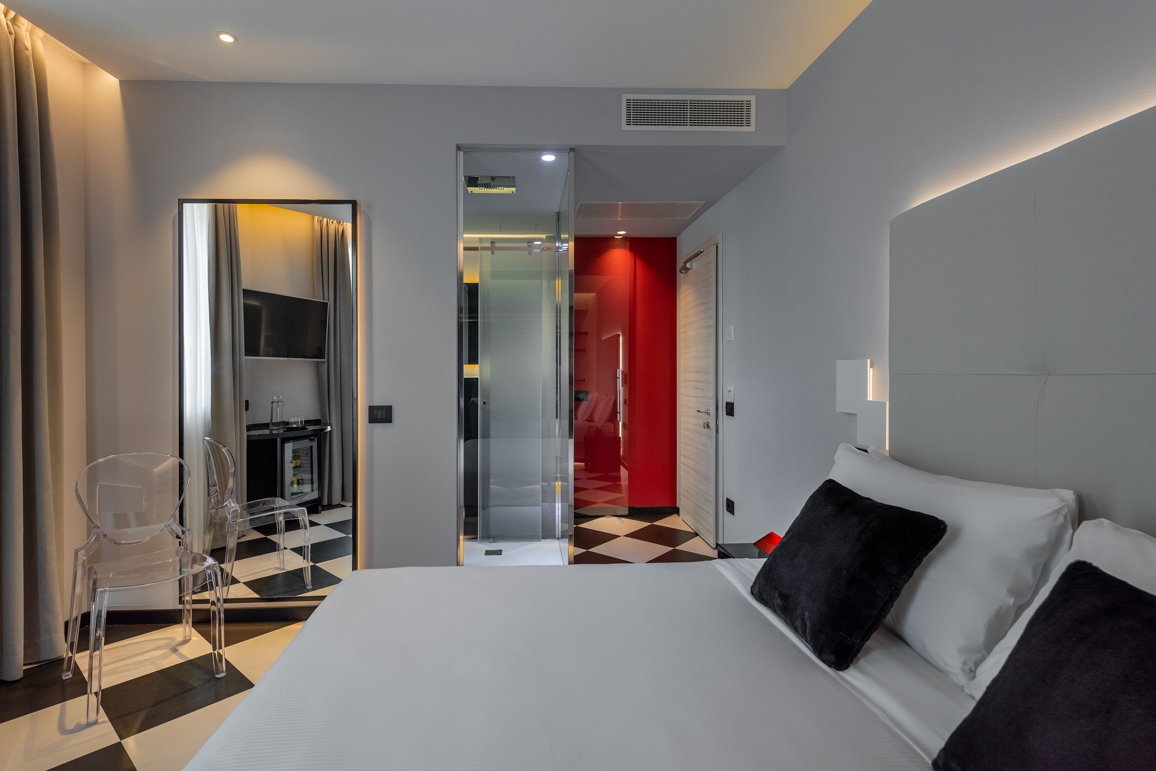Ein modernes Hotelzimmer mit einem großen Bett, einer Glassturzziehung, einer roten Tür und einem Schachbrettfußboden.