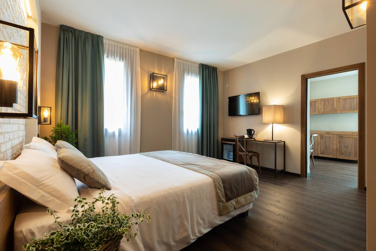 A hotel room with a large bed, a desk with a chair, a TV, and a wooden cabinet.