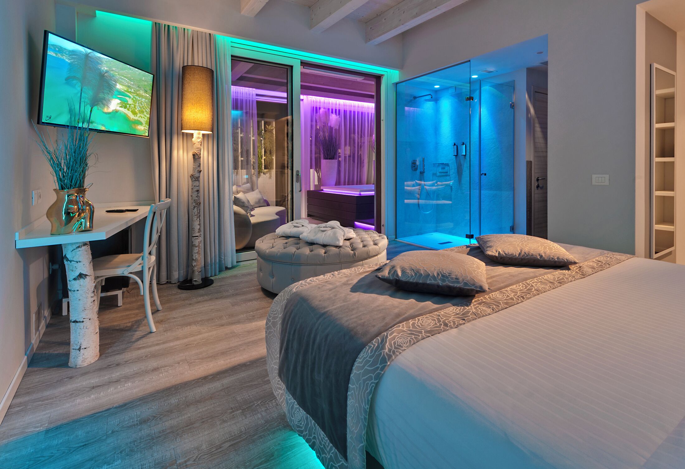 Un dormitorio moderno con cama, escritorio, televisor y baño con puerta de vidrio.