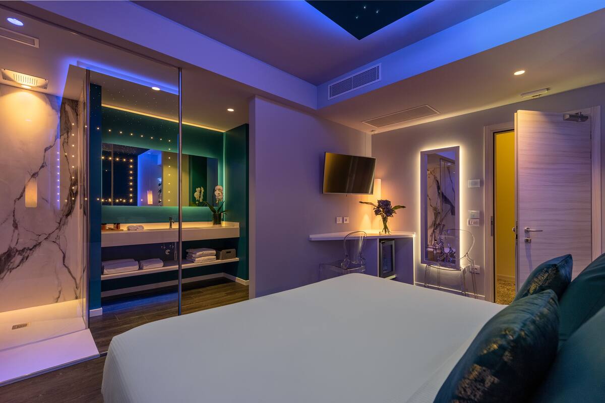 A modern bedroom with a large bed, a TV mounted on the wall, and a skylight.