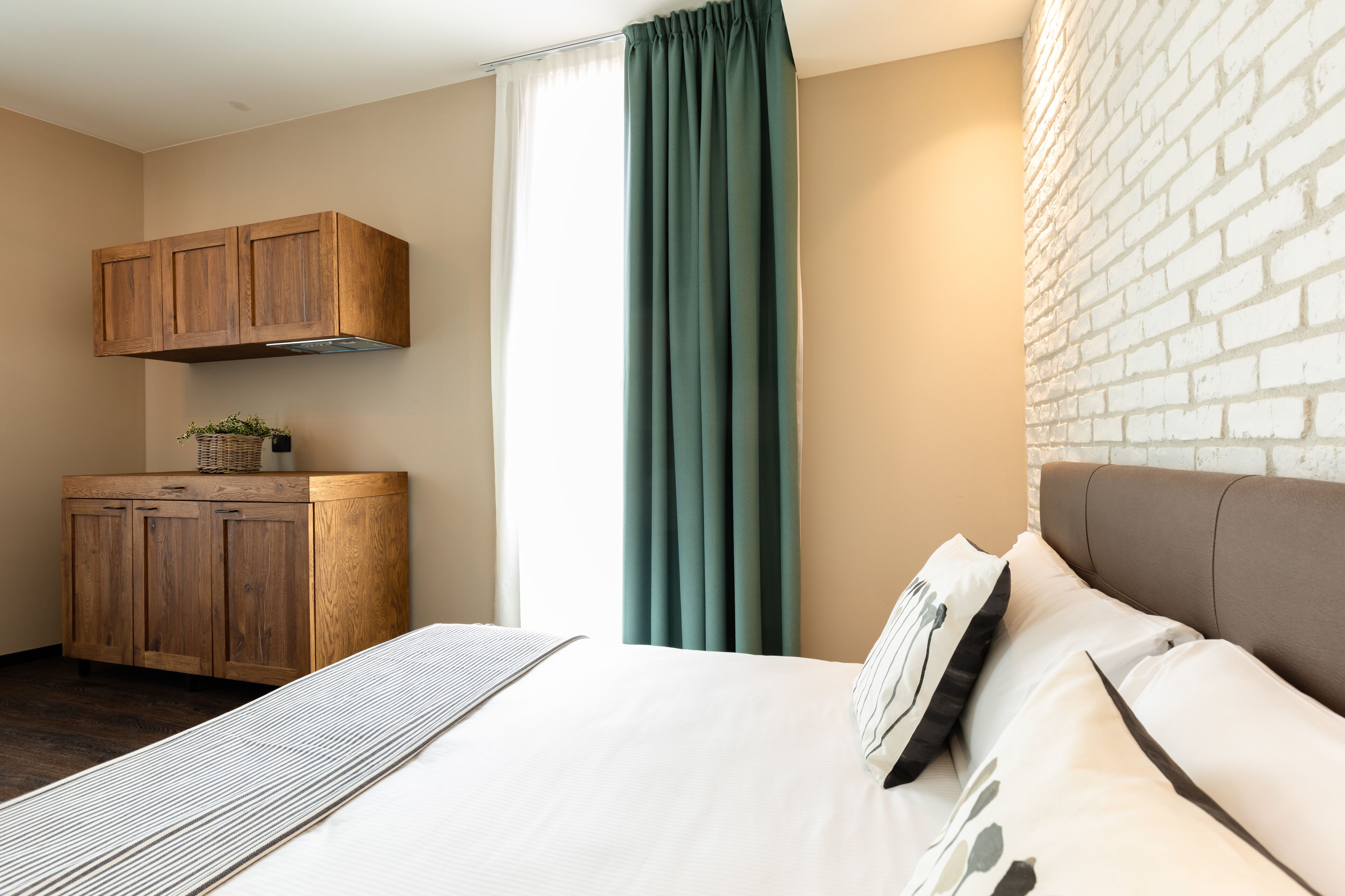 Une chambre à coucher avec un lit, une armoire en bois, une fenêtre avec des rideaux et un mur en briques.