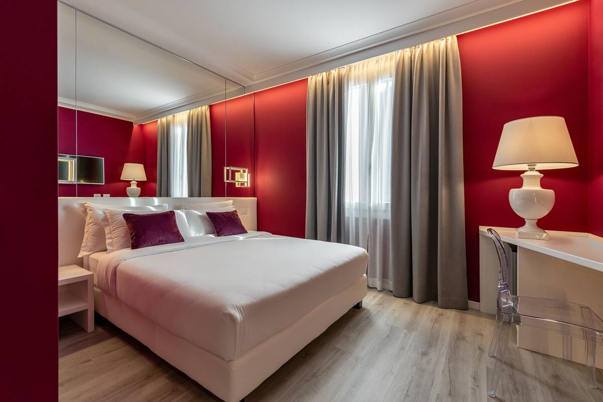 A modern hotel room with a large bed, bedside tables, a desk, and a mirror.