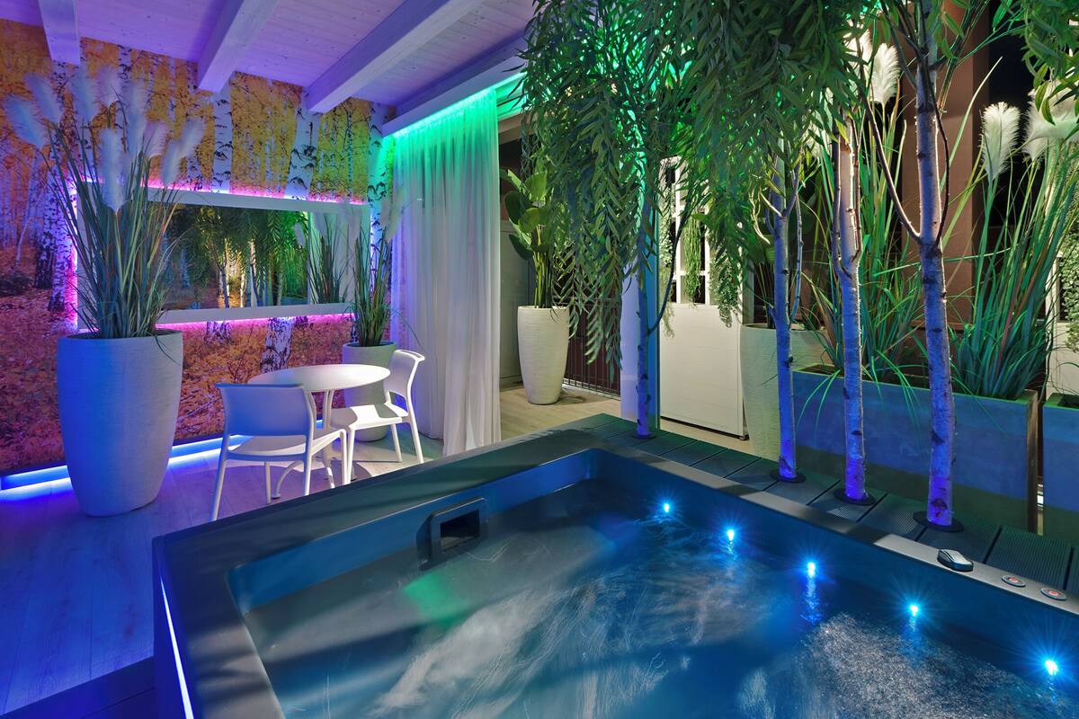 A modern indoor pool area with a hot tub, surrounded by potted plants and a seating area with a table and chairs.