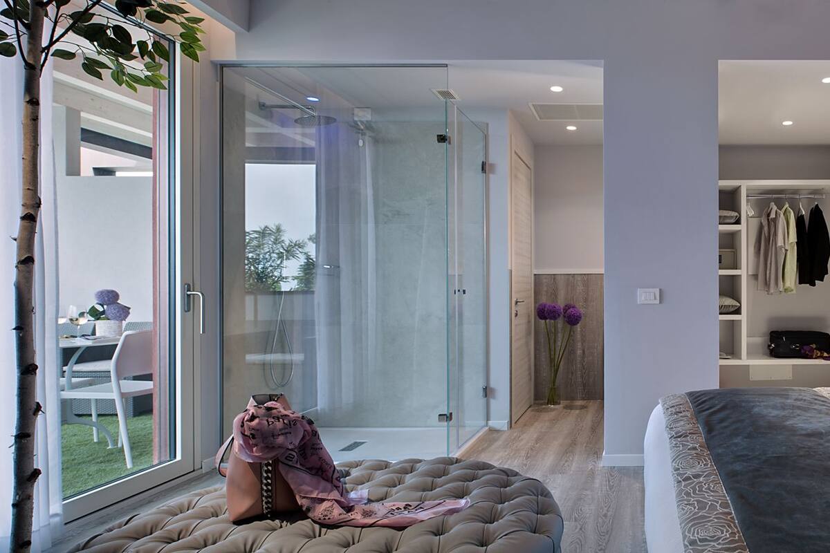 A modern bedroom with a large bed, a glass shower enclosure, and a walk-in closet.