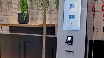 Un quiosco de autoservicio con pantalla táctil, una pequeña planta a su lado y piso de baldosas.