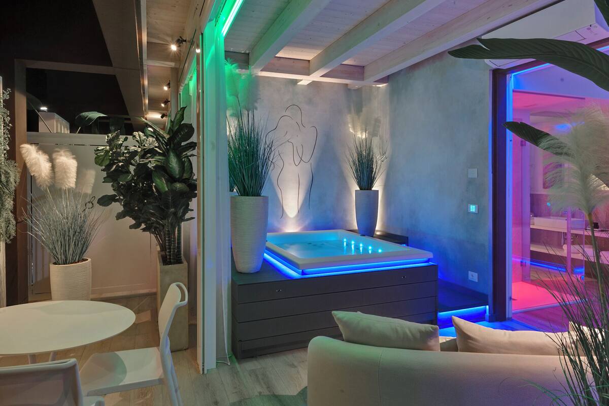 A modern spa room with a heated stone bath, surrounded by potted plants and a minimalist design.