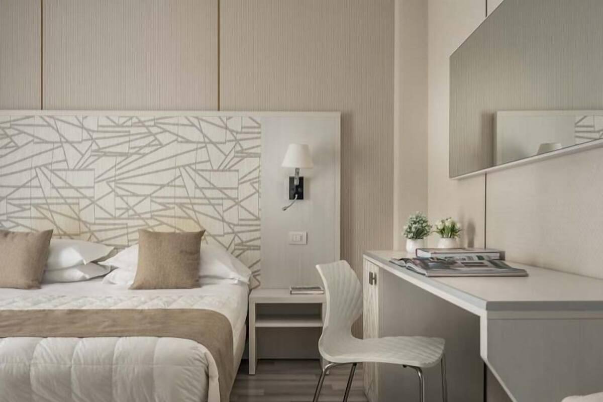 Een moderne hotelkamer met een bed, bureau, stoel en een wandlamp.