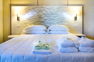 A hotel room with a large bed, two bedside tables, a headboard with geometric patterns, and two wall-mounted lamps.