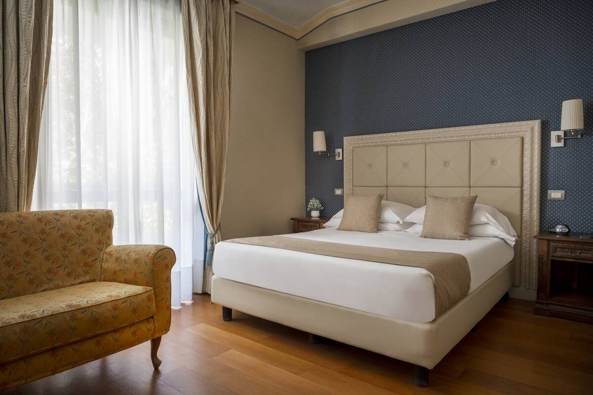 Een hotelkamer met een groot bed, een slaapbank en een nachtkastje met een lamp.