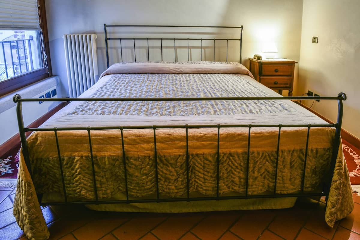 A single bed with a metal frame, a bedside table with a lamp, and a radiator.