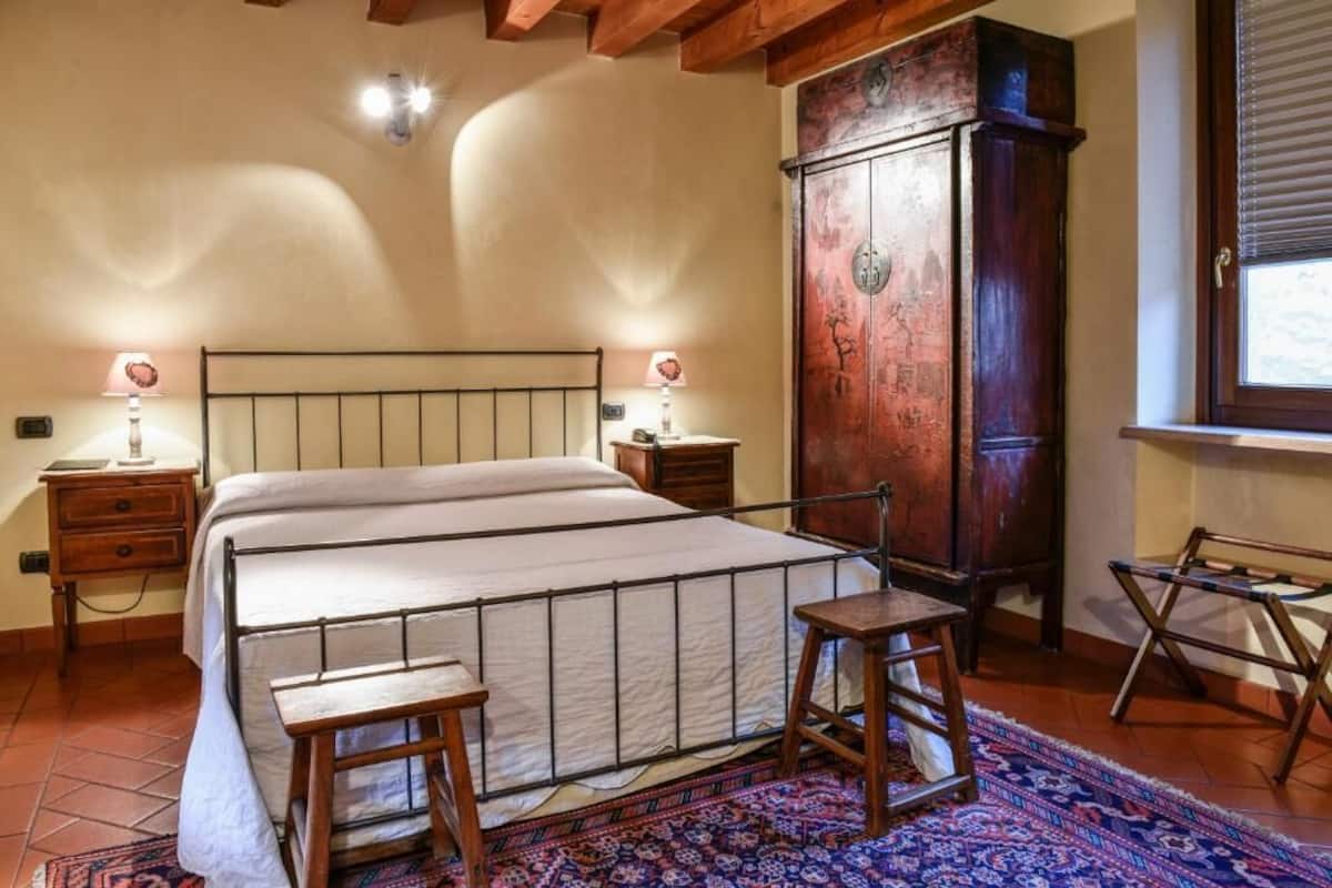 A bedroom with a large bed, wooden nightstands, a cabinet, and a window with blinds.