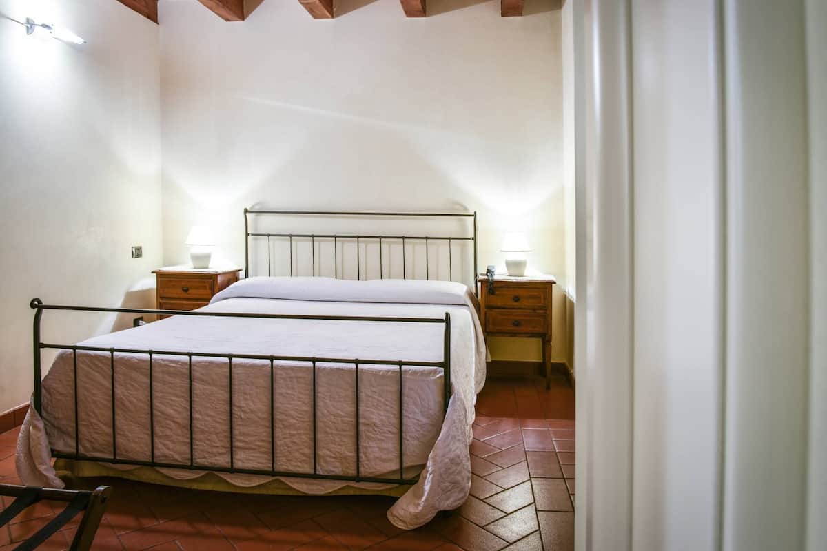 A single bed with a metal frame and white bedding in a room with tiled flooring and wooden furniture.