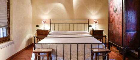 A bedroom with a large bed, two bedside tables, a wooden wardrobe, and a patterned rug.