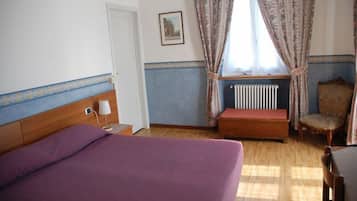 Una camera da letto con un letto, una sedia, un termosifone e una finestra con tende.