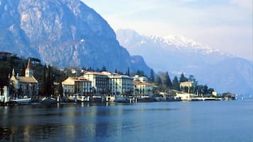 Une ville au bord d’un lac, avec des bâtiments qui bordent la rive, une église et des montagnes en arrière-plan.