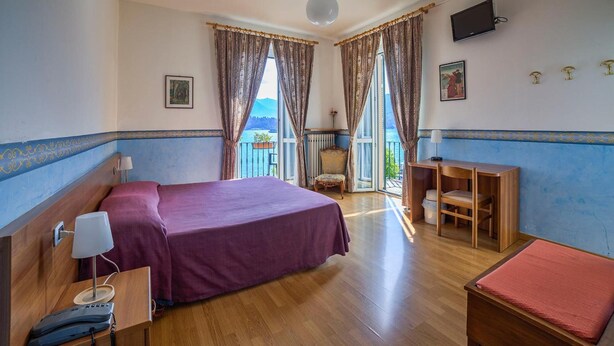 Habitación de hotel con cama, escritorio, silla, televisor y balcón con vistas.