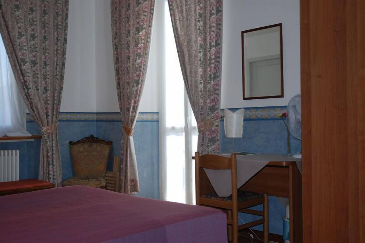 A room with a bed, a chair, a desk, a mirror, and a window with curtains.