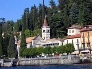 A coastal town with a prominent church tower, a bridge, and buildings with balconies overlooking the water.