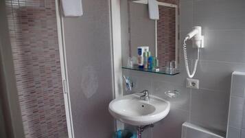 Un baño con lavamanos blanco, cabina de ducha con mampara de vidrio y espejo con una toalla colgando.