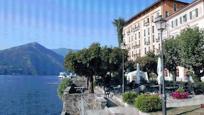 A waterfront promenade with stone steps, outdoor seating, and a row of buildings with balconies. - Hotel Riviera (Griante)