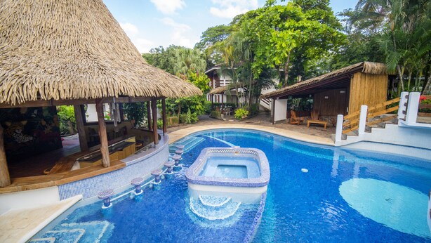 Una piscina con un jacuzzi, una zona de bar y una estructura de techo de paja.