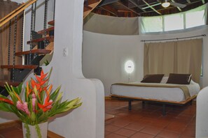 A bedroom with a bed, a nightstand, a wall-mounted light, and a staircase with a wooden railing. - Hotel Luna Llena (Tamarindo)