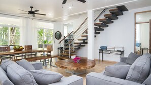 Una sala de estar moderna con sofás grises, una mesa de centro de madera y una escalera con barandilla de cristal.