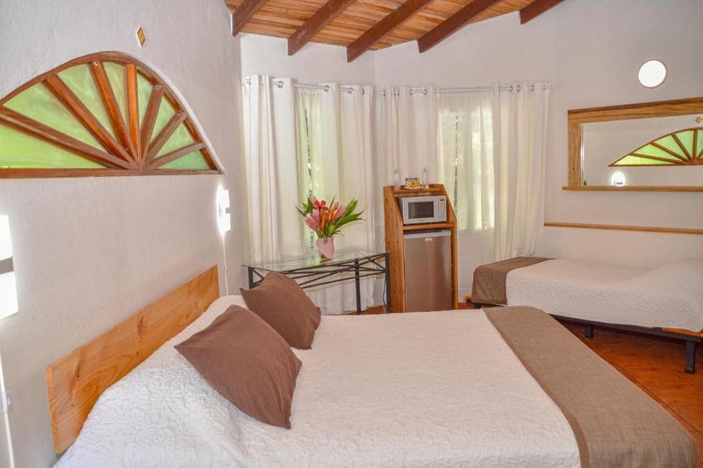 A hotel room with a bed, a desk with a microwave, and a mirror.