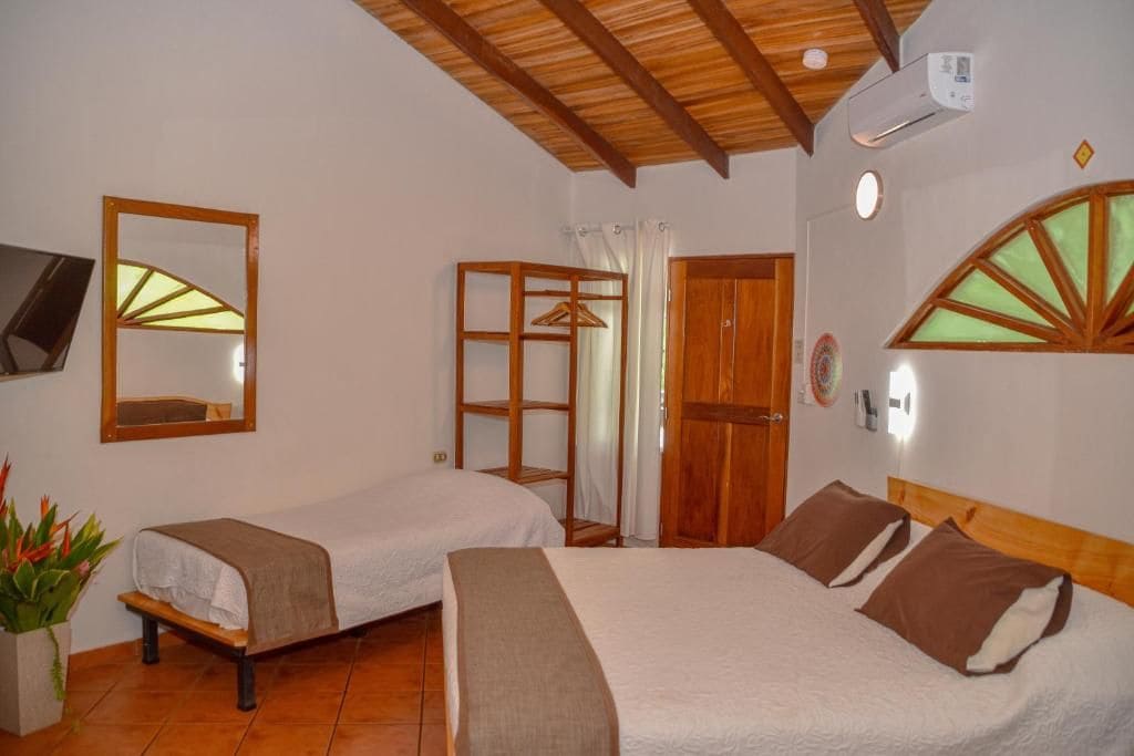 A hotel room with two beds, a wooden ceiling, a wall-mounted TV, and a window with a wooden frame.