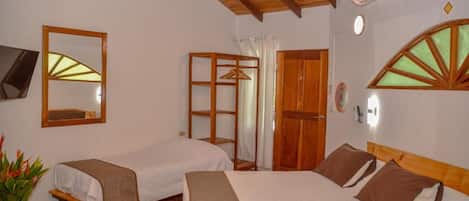 A hotel room with two beds, a wooden ceiling, a wall-mounted TV, and a window with a wooden frame.
